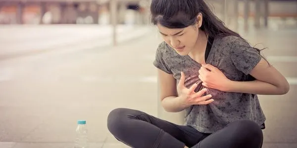A young woman sitting on the ground, holding her chest in pain, looking distressed as if suffering from sudden discomfort