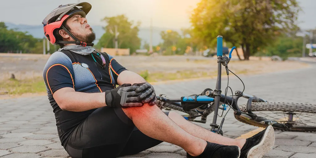 A cyclist sitting on the ground, holding his knee in pain. This suggests a knee injury