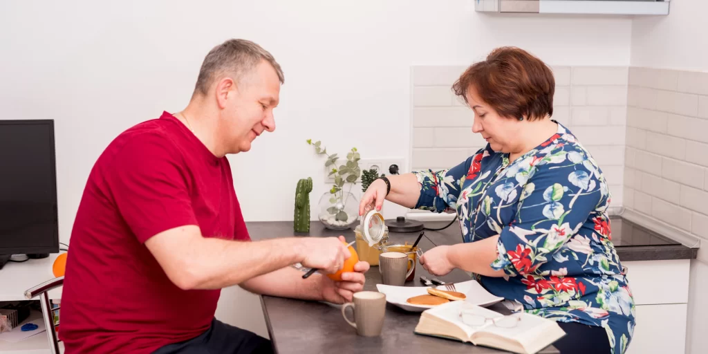 Middle-aged couple enjoying a healthy breakfast together at home, cutting fruits and pouring tea.