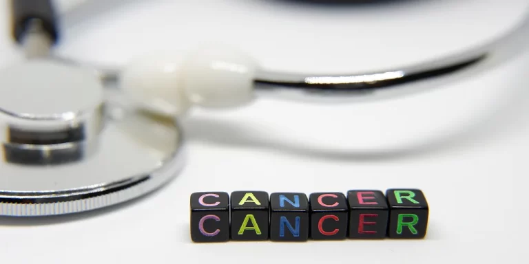 Colorful letter blocks spelling “CANCER” placed in front of a stethoscope on a white background, symbolizing medical care and cancer awareness.